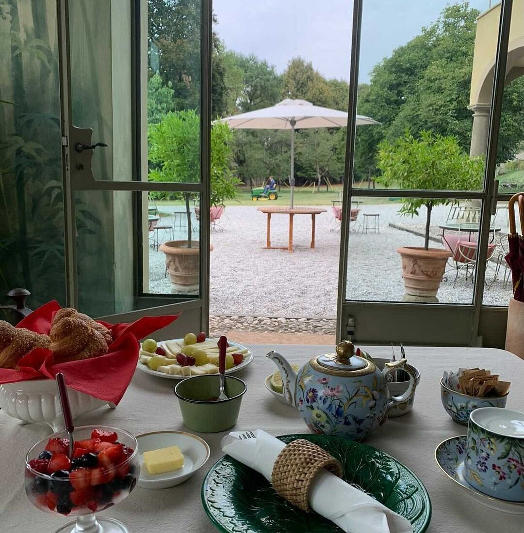 Breakfast of pastries, fruit and tea set by open garden doors looking onto the estate lawn