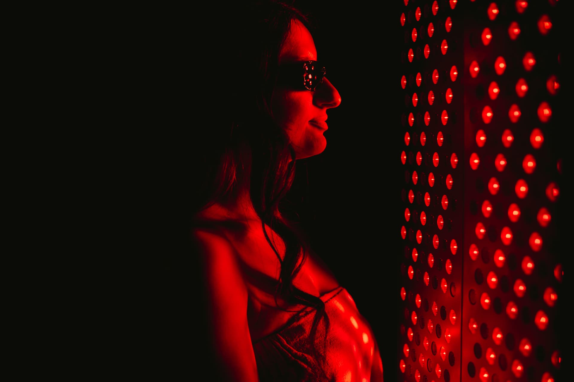 Guest in goggles standing beside a full-length red light therapy panel