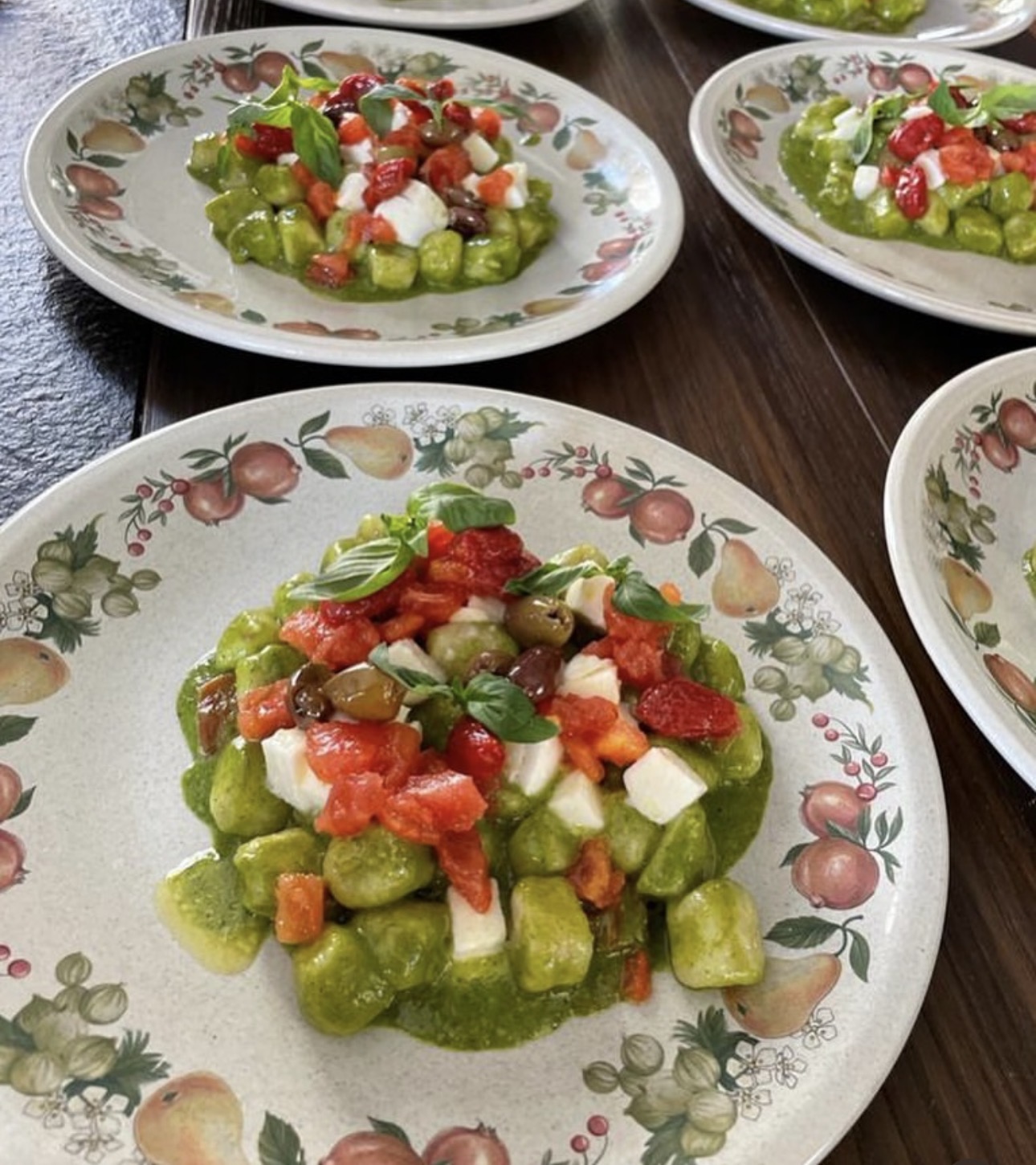 Plates of pesto gnocchi with mozzarella, olives and basil served to the group