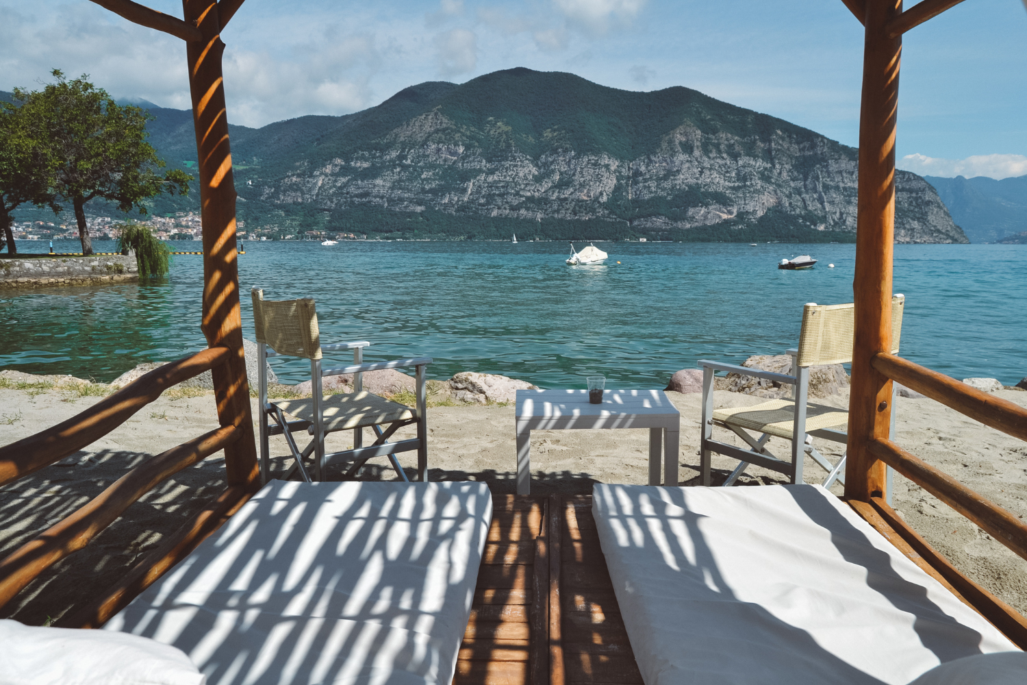 Shaded loungers on a private beach cabana looking across Lake Iseo to the mountains