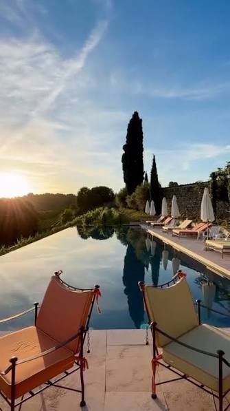 Infinity pool reflecting the sunset with loungers and a tall cypress on the terrace
